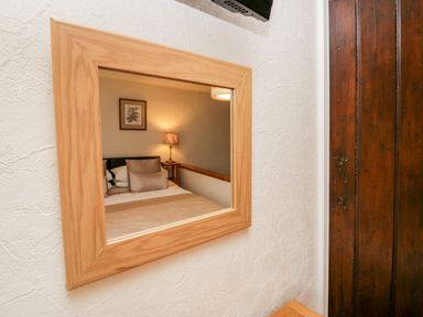 A mirror reflecting a bedroom with a bed pillows lamp and framed picture at Rusland View Rusland near Newby Bridge