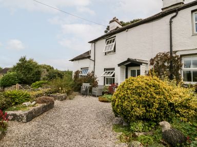 A garden with bushes and a gravel path outside a white house with open windows at Rusland View Rusland near Newby Bridge