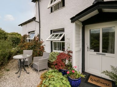 An outdoor seating area with two chairs and a round table beside a white house with open windows and potted plants at Rusland View Rusland near Newby Bridge