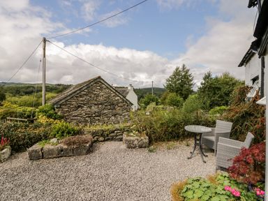 An outdoor seating area with two chairs and a table on a gravel surface near stone walls and greenery at Rusland View Rusland near Newby Bridge