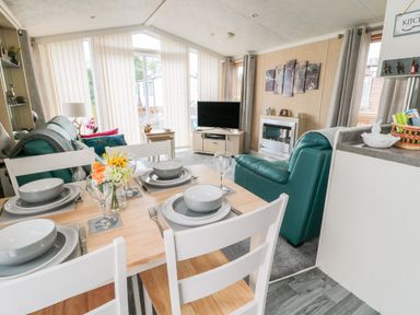 A dining table set with plates and glasses next to a living area with green chairs a TV and a fireplace at Ramblers Rest in Felton