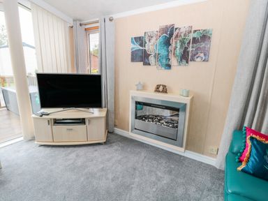 A living room with a television on a cabinet next to a modern fireplace and a teal sofa at Ramblers Rest in Felton