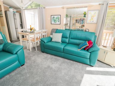 A living room with teal sofas a dining table set and a refrigerator at Ramblers Rest in Felton