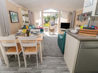 An open living and dining area with a dining table set with plates glasses and a bottle a green sofa a television and sliding glass doors leading outside at Ramblers Rest in Felton
