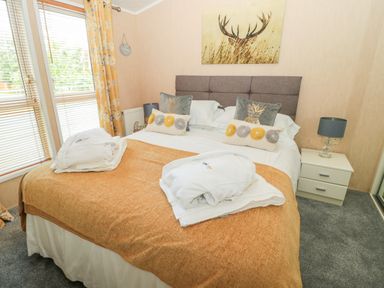 A bedroom with a double bed brown blanket and decorative pillows a bedside table with lamp and window with blinds and yellow curtains at Ramblers Rest Felton