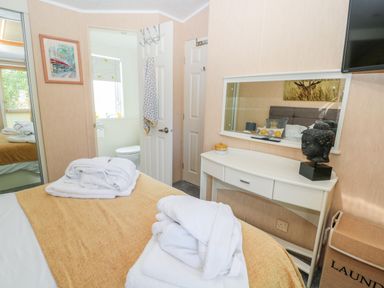 A bedroom with a bed covered by a yellow blanket and white towels with a dressing table a mirror a laundry basket and a door leading to a bathroom at Ramblers Rest in Felton