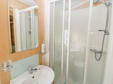 A bathroom with a sink, mirror, soap dispenser, and a shower cubicle with sliding glass doors at Ramblers Rest in Felton