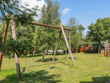 A wooden swing set on grassy land with trees and cabins in the background at Ramblers Rest in Felton