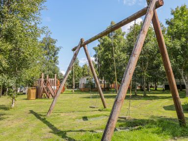 An outdoor area with wooden swings and a climbing structure surrounded by trees and grass at Ramblers Rest in Felton
