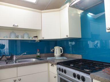 A kitchen with white cabinets a stainless steel sink a gas stove a kettle and blue backsplash at Ramblers Rest in Felton