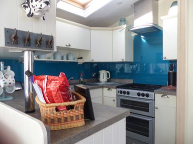 A kitchen with white cabinets a silver oven a woven basket with bags on the counter and blue backsplash at Ramblers Rest in Felton