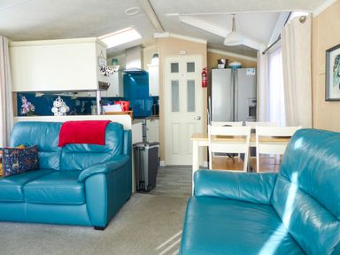 A living area with two blue sofas a dining table with chairs a kitchen with white cabinets and a silver refrigerator at Ramblers Rest in Felton