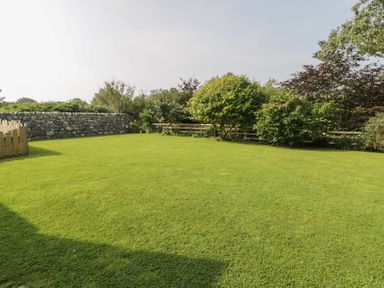 A grass lawn with trees and bushes surrounded by a stone wall and wooden fence at Tyn Ffynnon in Dyffryn Ardudwy