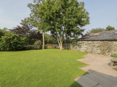A garden with grass, trees and stone wall next to a stone patio at Tyn Ffynnon in Dyffryn Ardudwy