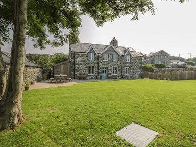 A stone house with a green lawn and trees in front at Tyn Ffynnon in Dyffryn Ardudwy