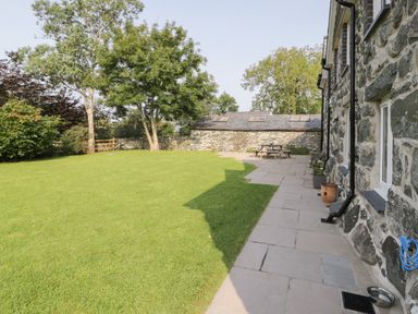 A garden with green grass stone patio and picnic table beside a stone house at Tyn Ffynnon in Dyffryn Ardudwy