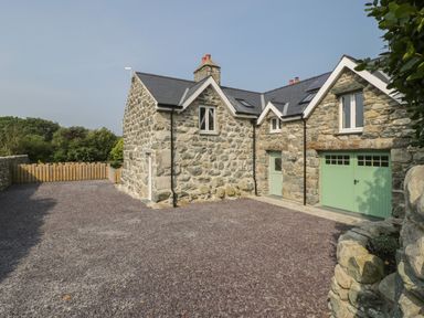 A stone house with a slate roof and green doors and windows with a gravel driveway and wooden fence at Tyn Ffynnon in Dyffryn Ardudwy