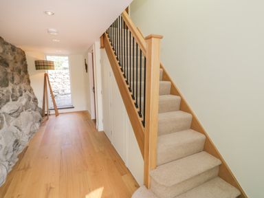 A hallway with wooden floor a stone wall a carpeted staircase and a floor lamp at Tyn Ffynnon in Dyffryn Ardudwy