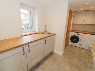 A utility room with washer and dryer under wood countertops and a small round sink under a window at Tyn Ffynnon in Dyffryn Ardudwy
