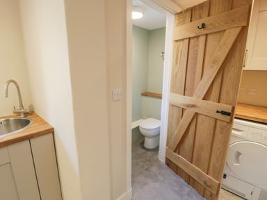 A utility room with a sink and a wooden door leading to a toilet at Tyn Ffynnon in Dyffryn Ardudwy