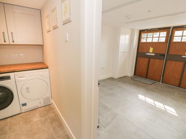 A laundry area with washer and dryer next to a room with double wooden doors and a tall white cabinet at Tyn Ffynnon in Dyffryn Ardudwy