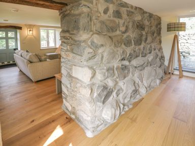 A living room with a stone wall wooden floor a floor lamp and a sofa at Tyn Ffynnon in Dyffryn Ardudwy