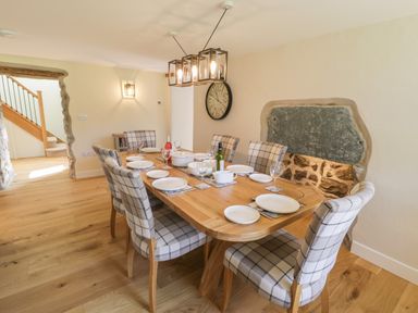 A dining room with wooden table and plaid chairs set for meal with plates and glasses at Tyn Ffynnon in Dyffryn Ardudwy