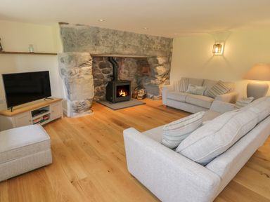 A living room with a stone fireplace wood stove two gray sofas a TV on a wooden stand and hardwood flooring at Tyn Ffynnon in Dyffryn Ardudwy
