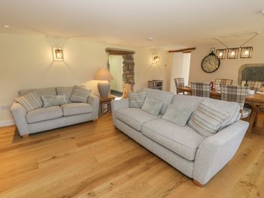 A living room with two gray sofas and pillows beside a wooden dining table with checked chairs at Tyn Ffynnon in Dyffryn Ardudwy