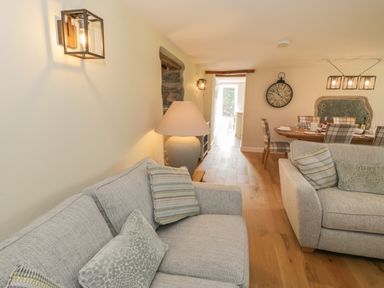 A living room with two sofas with cushions a lamp mounted wall lights wooden floor and a dining table with chairs at Tyn Ffynnon in Dyffryn Ardudwy