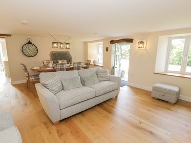 An open living and dining area with a sofa and cushions a dining table with chairs and an open door showing outside at Tyn Ffynnon in Dyffryn Ardudwy