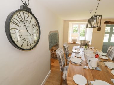 A dining room with a wooden table set for a meal and a large wall clock at Tyn Ffynnon in Dyffryn Ardudwy