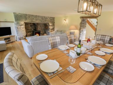 A dining table set with plates glasses and wine bottles in a room with a stone fireplace and sofas at Tyn Ffynnon in Dyffryn Ardudwy
