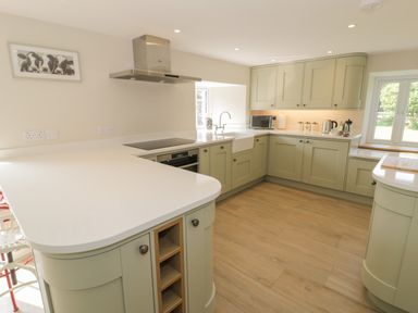 A kitchen with light green cabinets white countertops a sink stove microwave and window at Tyn Ffynnon in Dyffryn Ardudwy