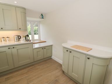 A kitchen with light green cabinets wooden flooring and a window at Tyn Ffynnon in Dyffryn Ardudwy