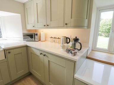 A kitchen countertop with a microwave kettle canisters and a French press and a window at Tyn Ffynnon in Dyffryn Ardudwy