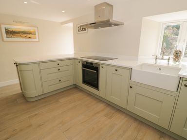 A kitchen with green cabinets a built in oven an induction cooktop a white farmhouse sink and a window at Tyn Ffynnon in Dyffryn Ardudwy
