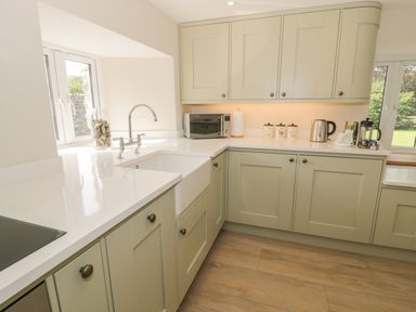 A kitchen with beige cabinets a white countertop a sink a microwave kettle and windows at Tyn Ffynnon in Dyffryn Ardudwy