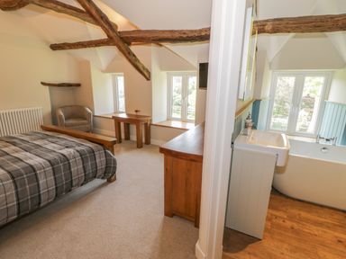A bedroom with a bed and armchair next to a small table and radiator with a bathroom containing a sink and bathtub visible through a doorway at Tyn Ffynnon in Dyffryn Ardudwy
