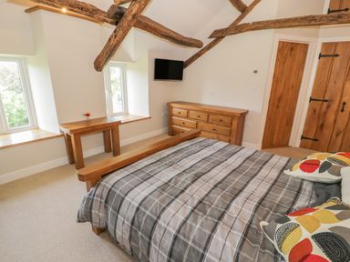 A bedroom with a bed a wooden dresser a small table and wooden beams on the ceiling at Tyn Ffynnon in Dyffryn Ardudwy