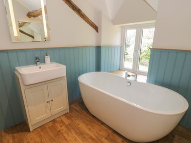 A bathroom with a freestanding bathtub a sink with cabinet a mirror and a window at Tyn Ffynnon in Dyffryn Ardudwy