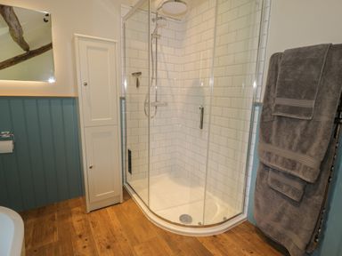 A bathroom with a glass shower enclosure white tiled walls a white cabinet and grey towels hanging at Tyn Ffynnon in Dyffryn Ardudwy