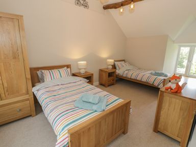 A bedroom with two single beds nightstands lamps wardrobe and a window at Tyn Ffynnon in Dyffryn Ardudwy