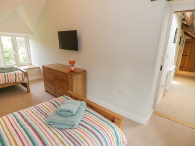 A bedroom with two single beds striped bedding wooden dresser with a fox plush toy and a wall mounted television at Tyn Ffynnon in Dyffryn Ardudwy