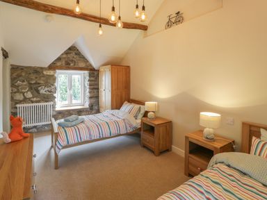 A bedroom with two single beds striped bedding wooden furniture and a stone wall at Tyn Ffynnon in Dyffryn Ardudwy