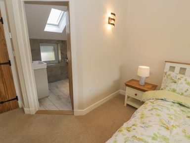A bedroom with a bed and nightstand with a lamp and an adjacent bathroom with a skylight at Tyn Ffynnon in Dyffryn Ardudwy