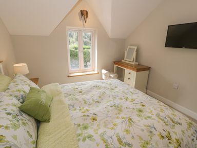 A bedroom with a bed a side lamp a window a dressing table and a wall mounted tv at Tyn Ffynnon in Dyffryn Ardudwy