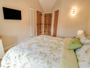 A bedroom with a floral bedspread a green pillow a wall-mounted TV three wooden doors a wall radiator and a bedside lamp at Tyn Ffynnon in Dyffryn Ardudwy