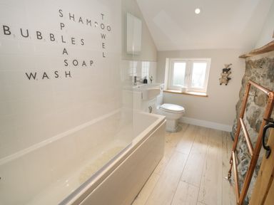A bathroom with a bathtub with words on the tiles a toilet a sink and a window at Tyn Ffynnon in Dyffryn Ardudwy