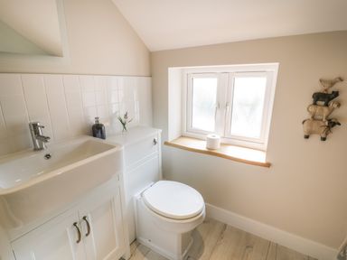 A bathroom with a white sink and cabinet a toilet a window with a toilet paper roll on the sill and wall decorations at Tyn Ffynnon in Dyffryn Ardudwy